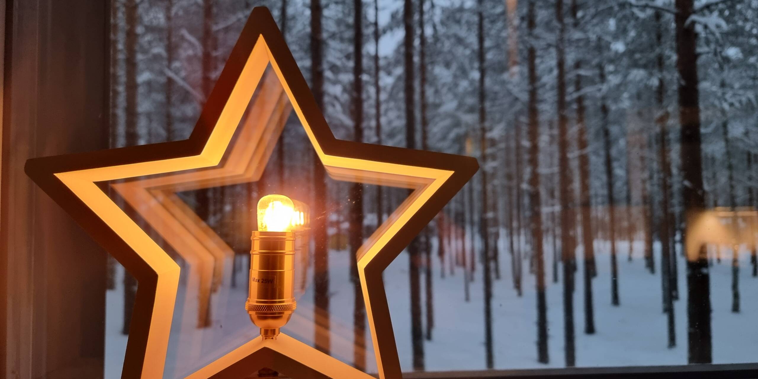 Ikkunalla puinen tähti jonka keskellä lamppu. Ulkona hämärää