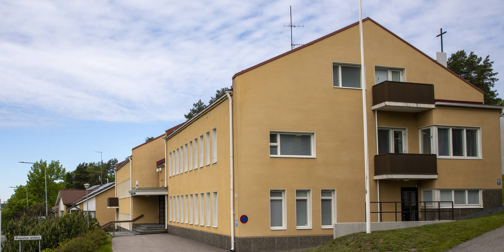 Keltainen kirkkorakennus, jossa on useita ikkunoita ja parvekkeita. Edessä on kävelytie ja puutarha. Taustalla näkyy sininen taivas ja pilviä.