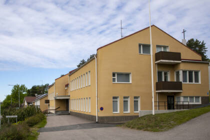 Keltainen kirkkorakennus, jossa on useita ikkunoita ja parvekkeita. Edessä on kävelytie ja puutarha. Taustalla näkyy sininen taivas ja pilviä.