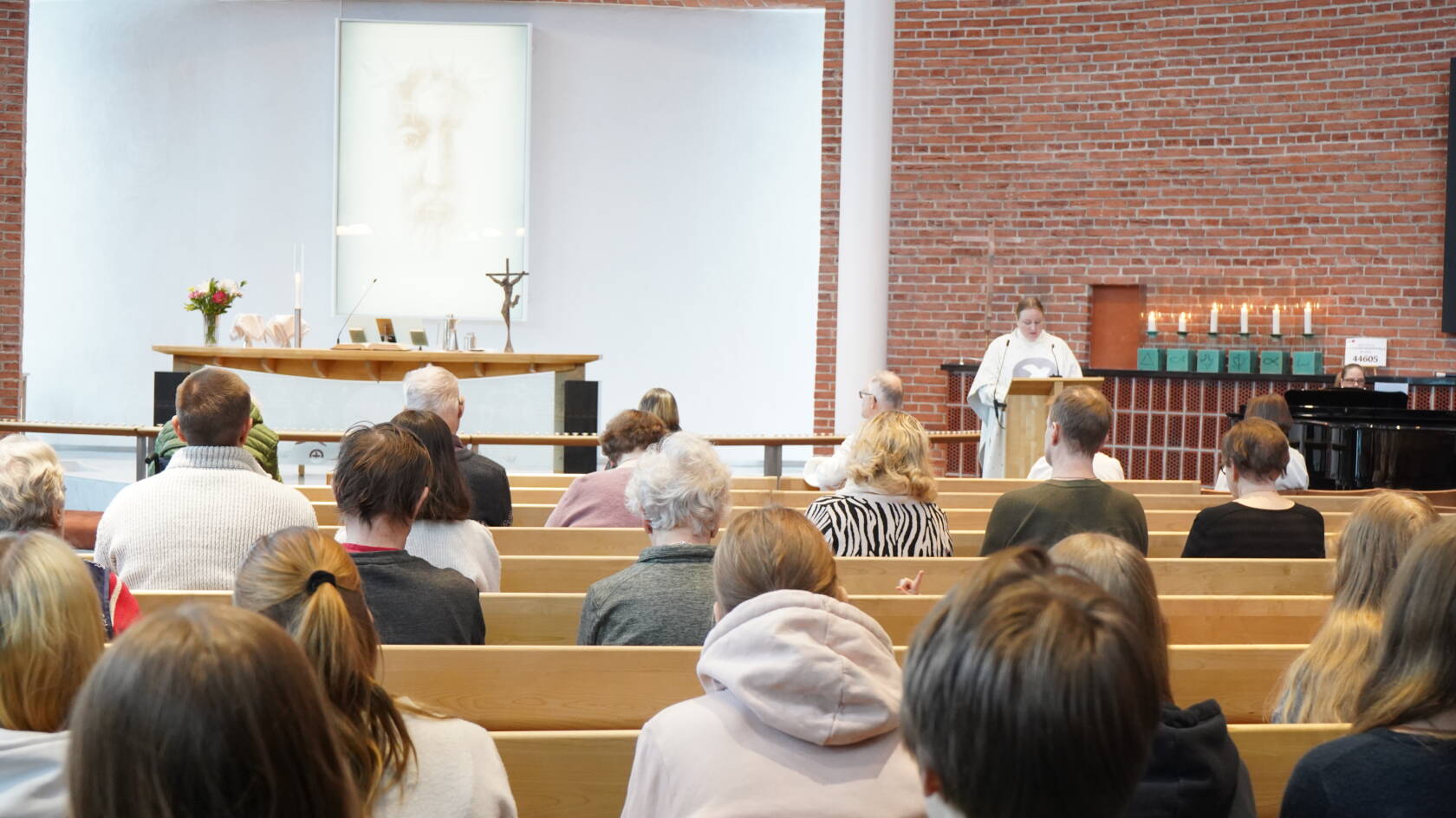 IHmisiä Atilahden kirkkosalissa istumassa. kuva otettu salin takaa. Pappi lukupuletissa puhumassa.