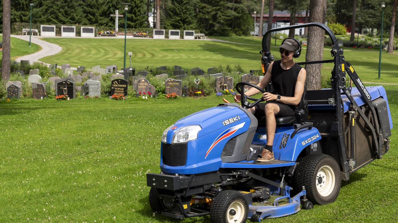 Nuori henkilö ajaa ruohonleikkuria hautausmaalla.