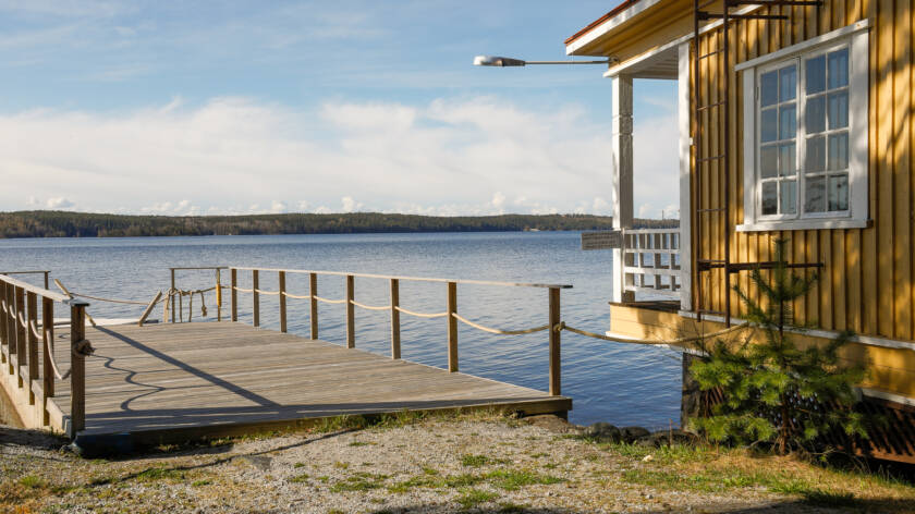 kaunis järvimaisema, jossa on laituri ja keltainen rantasauna.