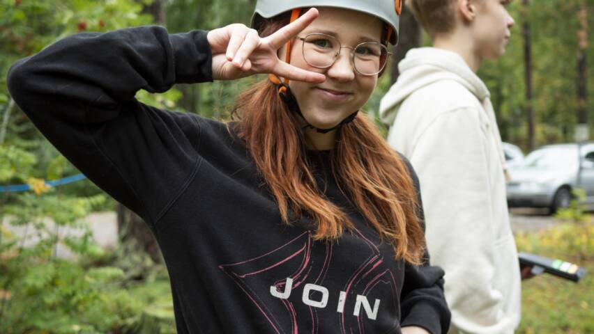 Henkilö poseeraa kiipeilykypärä ja valjaat päällä