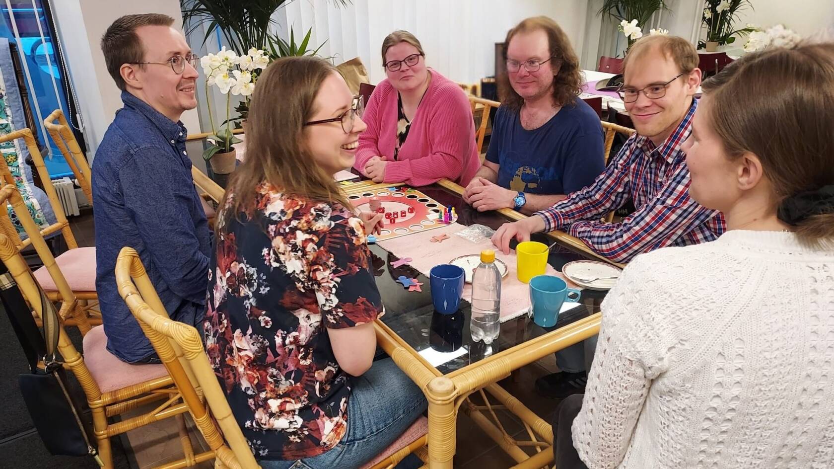 Työikäisiä henkilöitä juttelee pöydän ääressä iloisesti.