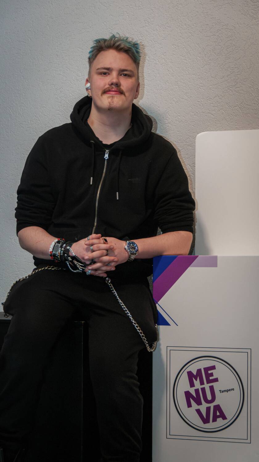 Henkilö poseeraamassa pöydän vieressä, kyltissä lukee: menuva