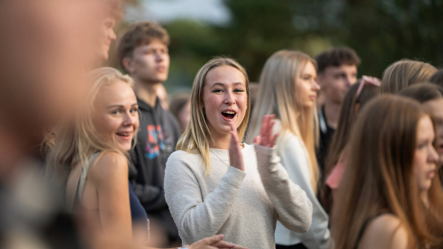 Nuoria ihmisiä on kokoontunut ulos, yksi tyttö keskellä hymyilee ja taputtaa innokkaasti.