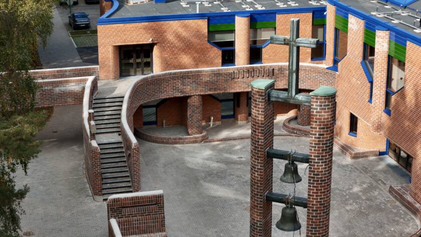 The red-brick bell tower of Hervanta Church and the church entrance area seen from above. The tower has two bells and a cross at the top.
