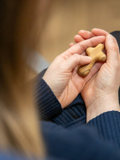A person holding wooden cross in hands.
