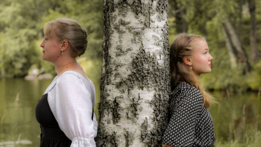 Näkymätön duo kesäisessä maisemassa. Kaksi naista nojaavat saman koivun runkoon katsoen eri suuntiin