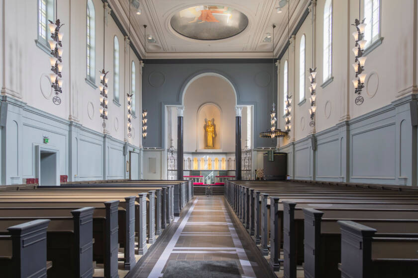 Interior of Viinikka Church seen from the central aisle. Dark wooden pews lead towards the altar, with a golden sculpture above it.