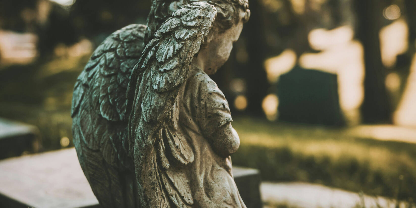 An angel statue in a cemetery, with gravestones and trees in the background.