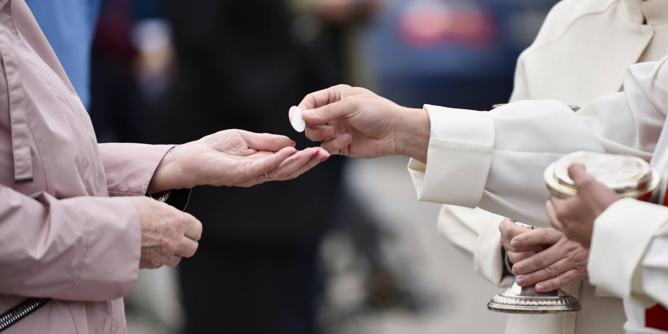 Two hands: one offering Holy Communion, the other receiving it.