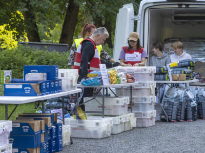 Avustustyöntekijöitä jakamassa tavaroita ulkona. Taustalla pakettiauto ja pöydät täynnä laatikoita ja tarvikkeita.