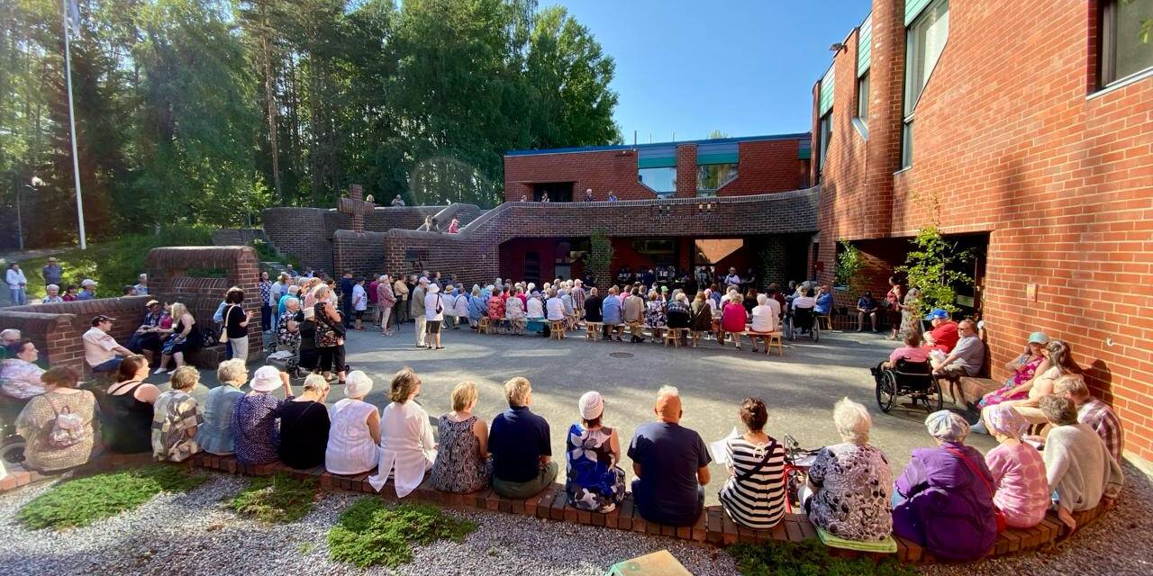 Joukko ihmisiä on kerääntynyt Hervannan kirkon sisäpihalle kauniina kesäitana.