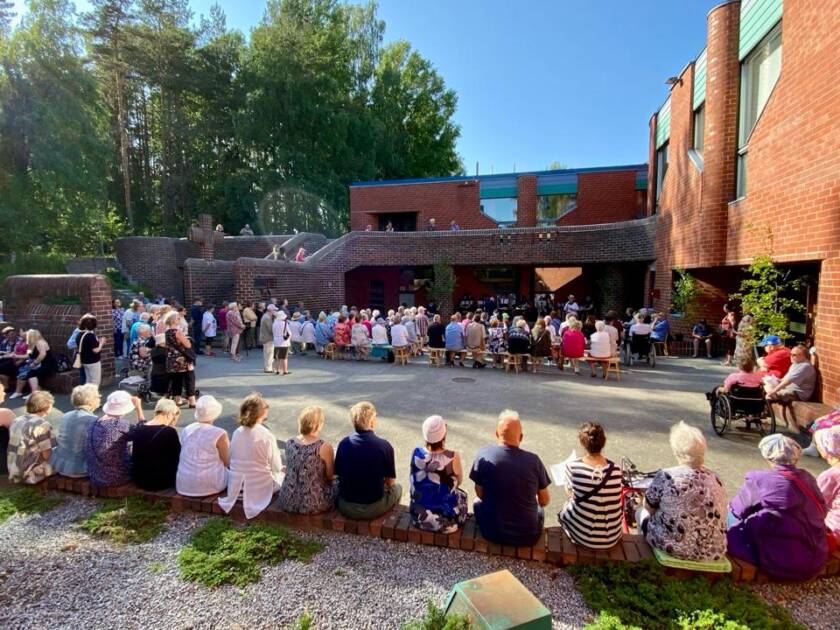 Joukko ihmisiä on kerääntynyt Hervannan kirkon sisäpihalle kauniina kesäitana.