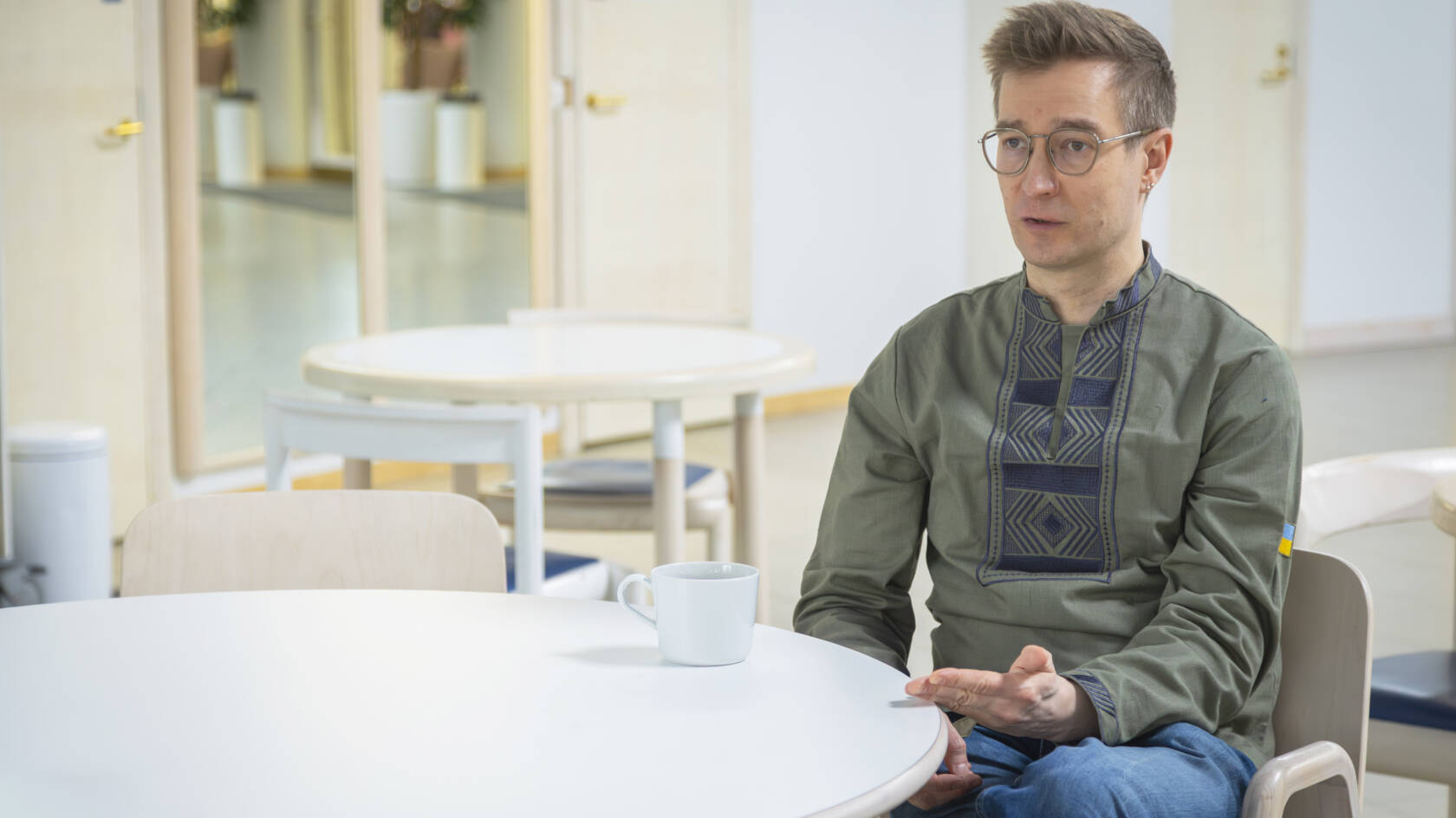 Henkilö istuu pyöreän pöydän ääressä kuppi edessään.
