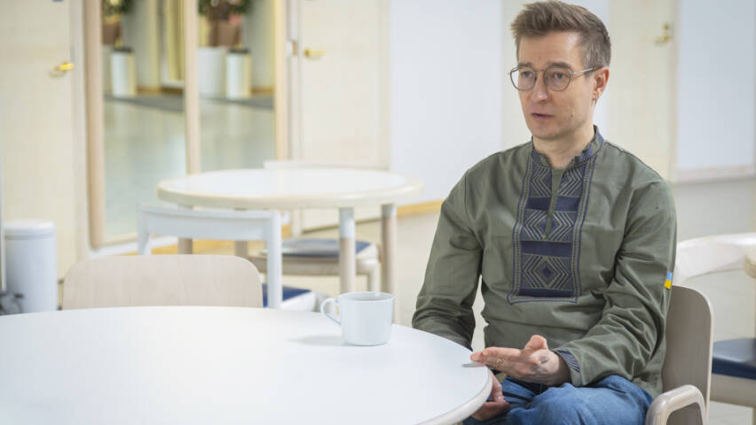 Henkilö istuu pyöreän pöydän ääressä kuppi edessään.