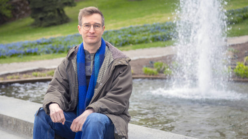 Suihkulähteen reunalla istuu ihminen, jolla on kaulaliina ja takki päällä.