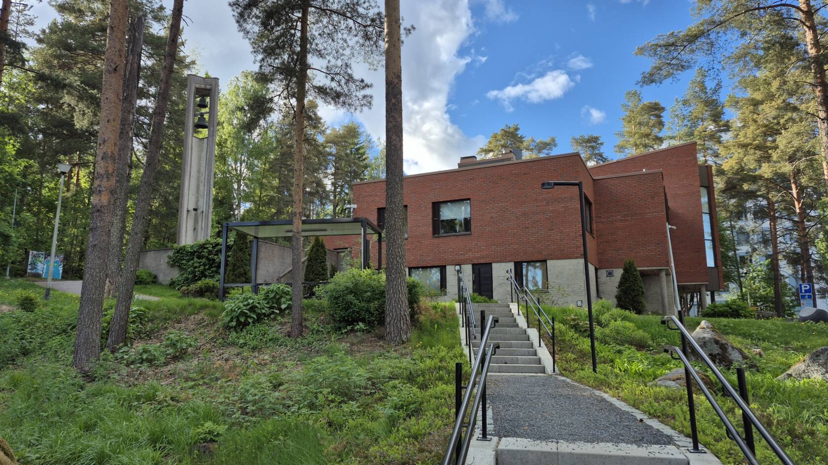 Tesoman kirkko eteläpuolelta kuvattuna keväällä vehreän luonnon ja mäntyjen keskellä.