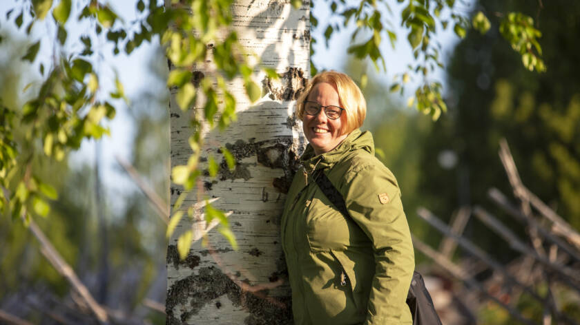 Vihreään takkiin pukeutunut henkilö nojaa vartalollaan koivun runkoon.
