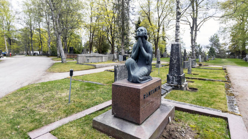 Iso hautamuistomerkki, jossa päällimmäisenä on leukansa alle rukousasentoon kätensä kohottaneen, yhden polven varaan polvistuneen naishahmon patsas.