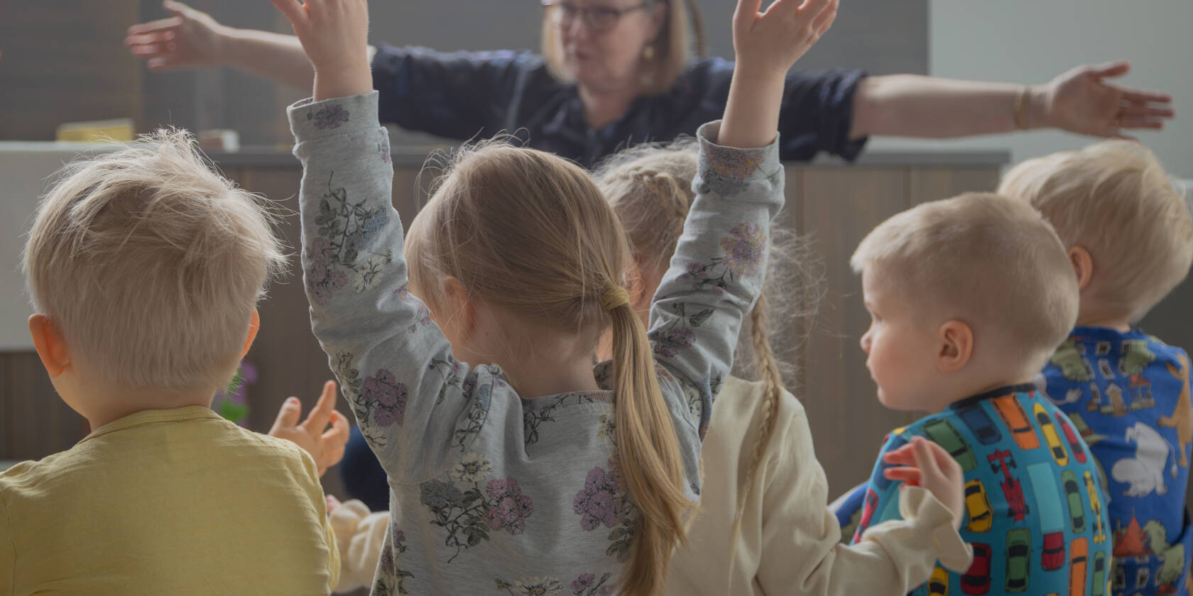 Lapsia istuu penkillä selin kameraan. Yksi lapsista nostaa kädet ilmaan.