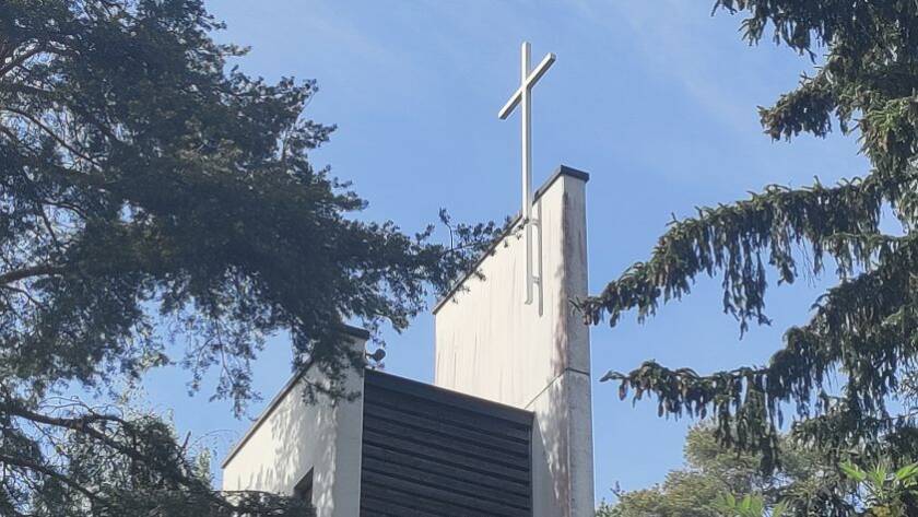 The tall white cross of Lielahti Church rises above the church roof among the trees.