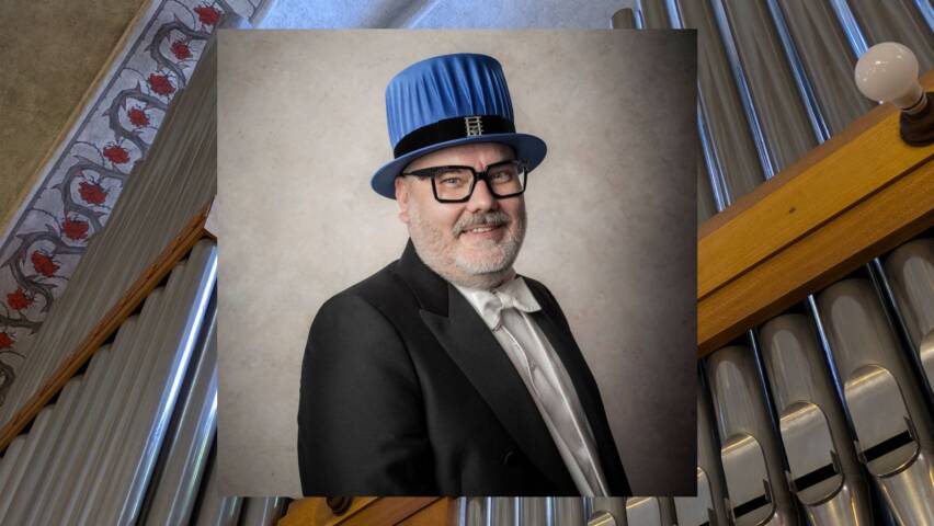 Kuvassa on mies musiikin tohtorin juhla-asussa hattuineen. Taustalla urkujen julkisivu.
