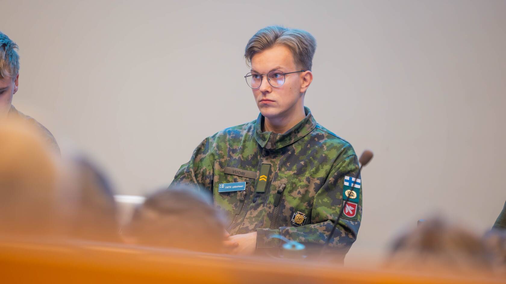 Armeijan maastopukuun pukeutunut nuori mies istuu pöydän ääressä