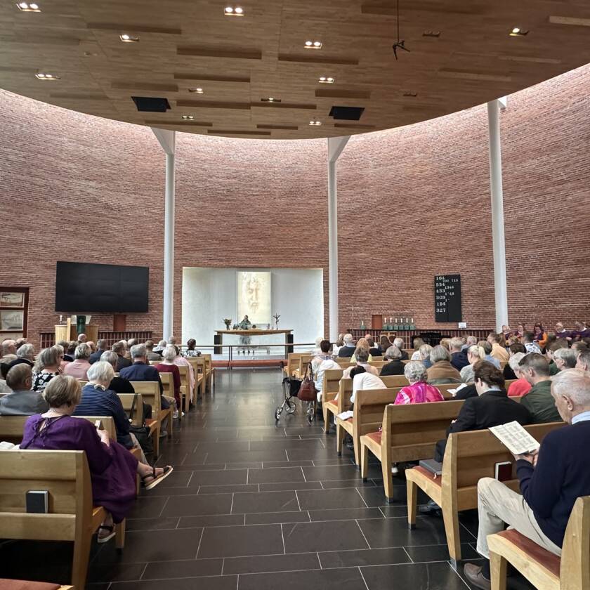 Sisäkuva AItolahden kirkon kirkkosalista. Kirkossa paljon ihmisiä istumassa. Kuva otettu takaa päin.