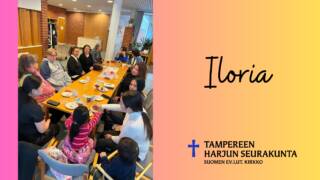 Ihmisiä pitkän pöydän ympärillä sisätiloissa. Teksti: Iloria, kelta-pinkki tausta