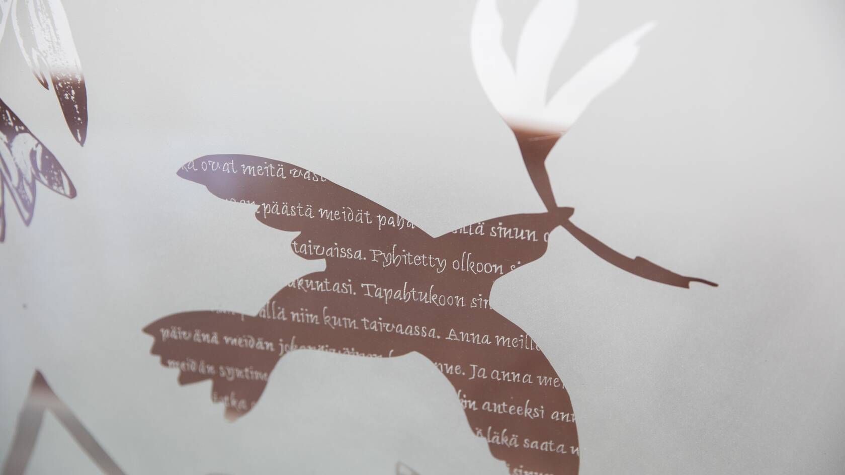 Lasikoristelussa kuva kyyhkystä, sekä Isä meidän -rukouksen tekstiä.