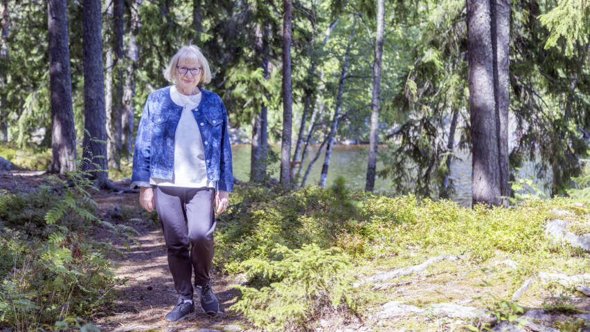 Henkilö kävelee aurinkoista polkua pitkin metsässä.