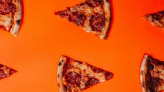 Pizzasiivuja kirkkaan oranssilla taustalla.