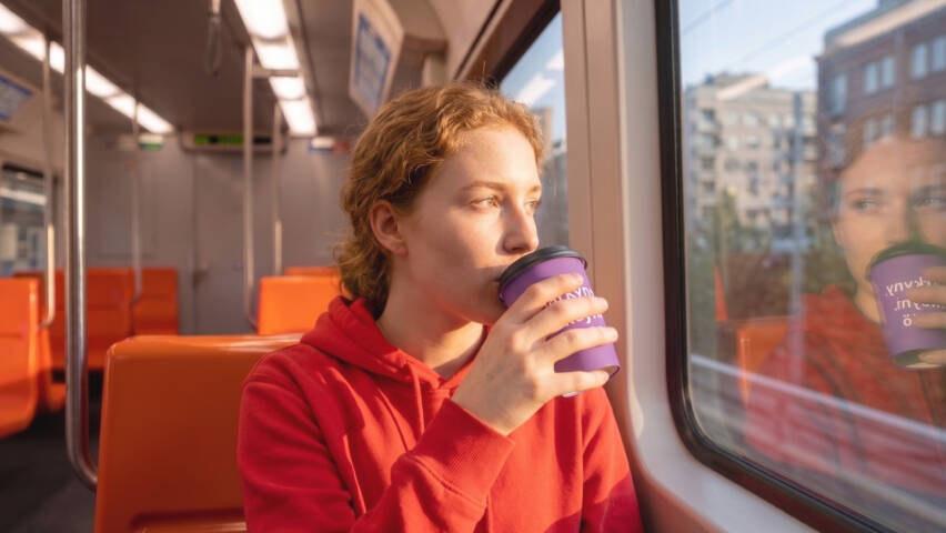 Henkilö juo kahvia violetista kupista junassa, katsoen ulos ikkunasta.