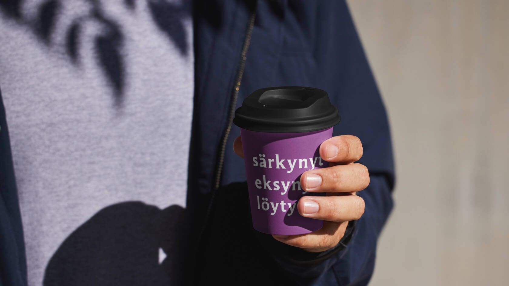 Mies pitää violetista kahvikupista, jossa on teksti "särkynyt eksynyt.