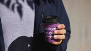 Mies pitää violetista kahvikupista, jossa on teksti "särkynyt eksynyt.