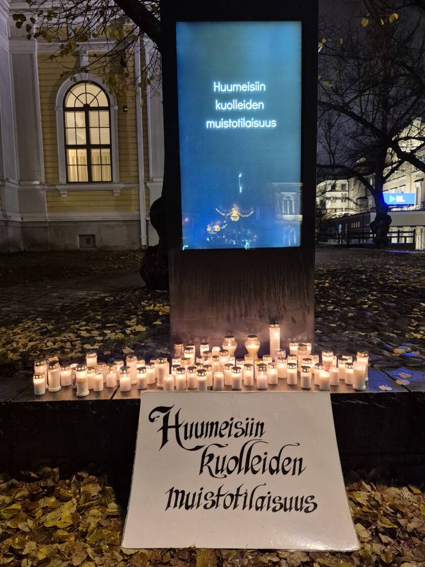 Kirkon edustalla pimeässä valotaulussa ja kyltissä teksti: Huumeisiin kuolleiden muistotilaisuus.