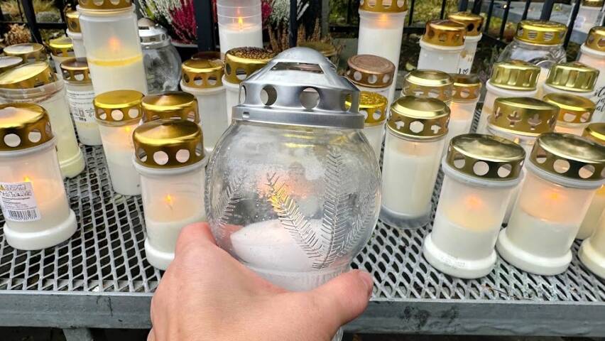 Etualalla käsi laittamassa kynttilää ritilälle, jossa paljon sytytettyjä hautakynttilöitä