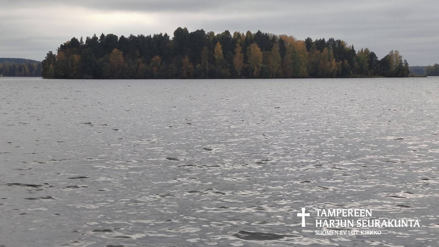Syksyinen saari. Harmaata taivasta, etualalla paljon harmaata vettä.
