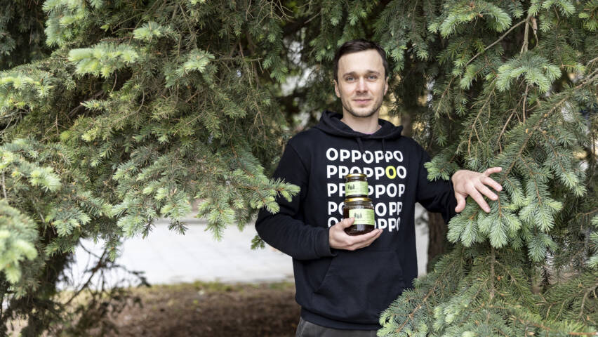 Henkilö seisoo kuusen katveessa ja pitää oikeassa kädessään kahta lasipurkkia.