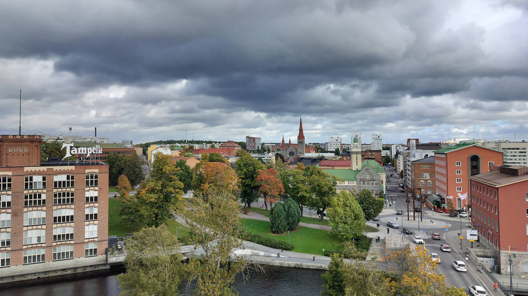 Kaupunkimaisema, jonka yllä on tummia pilviä. Kaukana näkyy kirkon torni.