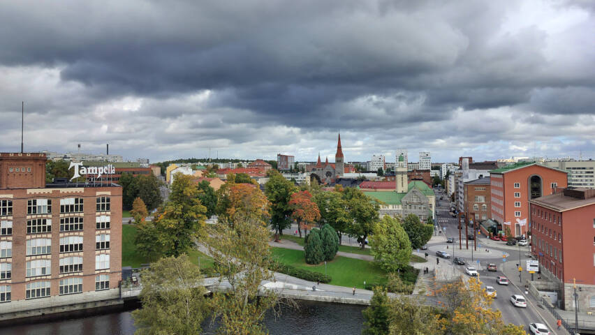 Kaupunkimaisema, jonka yllä on tummia pilviä. Kaukana näkyy kirkon torni.